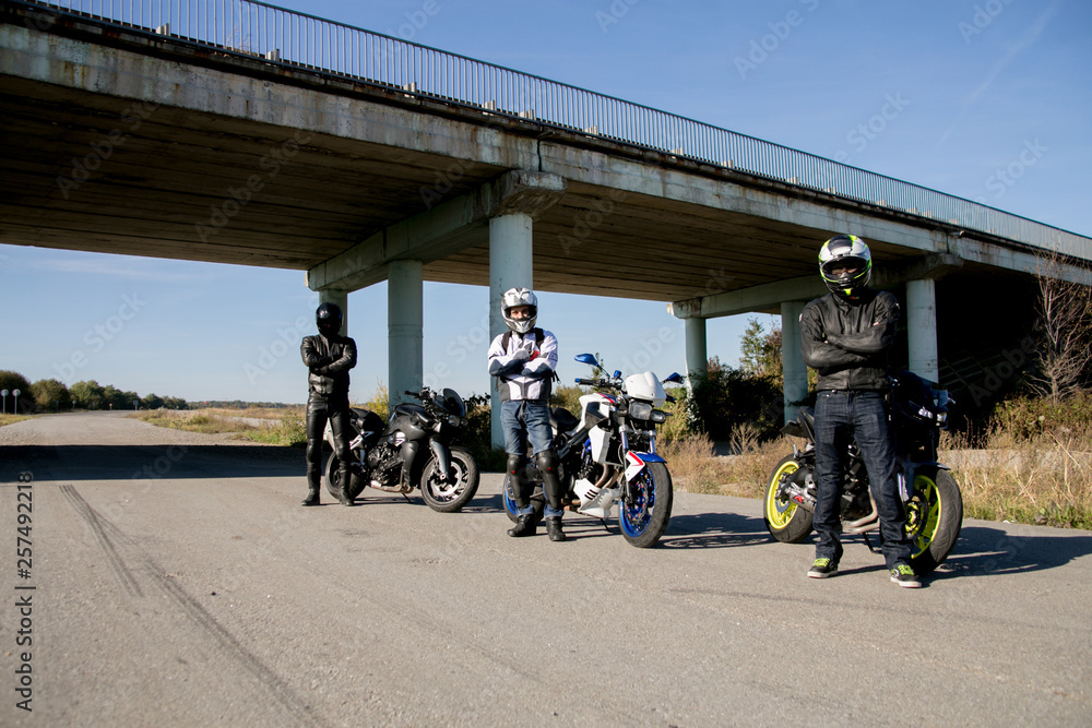 Tree motorcyclists in helmets Journey to a motorcycles. Motorcyclists stands on the road Tree motorcyclists in helmets Journey to a motorcycles. Motorcyclists stands on the road