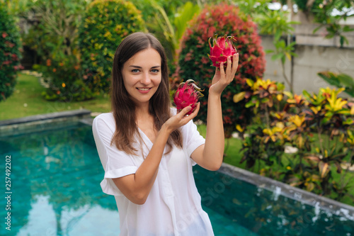 Happy girl with beautiful smile holds two dragon fruits  pitaya in her hands background of pool
