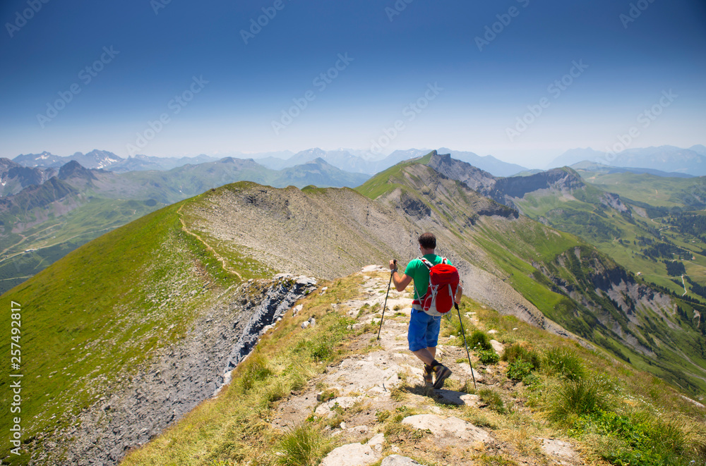 A solo male hiker descending a steep mountain ridge near Mont Joly in France, halfway the Tour du Mont Blanc. A solo male hiker descending a steep mountain ridge near Mont Joly in France, halfway the Tour du Mont Blanc.