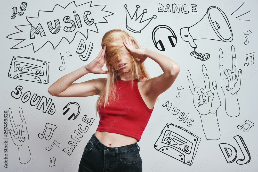 Funky mood. Close up portrait young woman in red tank top covering face with her hair while standing against grey background with music theme doodles. Funky mood. Close up portrait young woman in red tank top covering face with her hair while standing against grey background with music theme doodles.