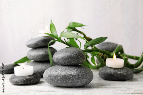 Zen stones, bamboo and lighted candles on table against light background