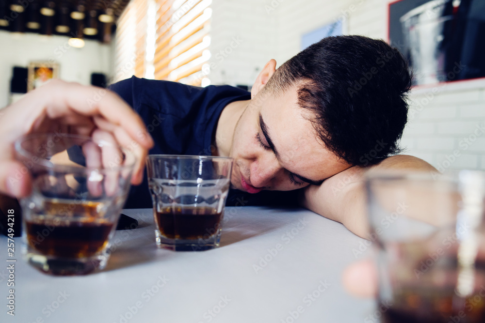 Young man drunk at bar drinking alcohol whiskey sleeping