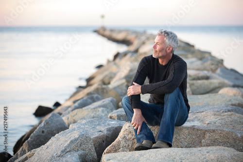 Gray-haired man contemplating on coastal rocks at dusk, Dennis, Massachusetts, USA