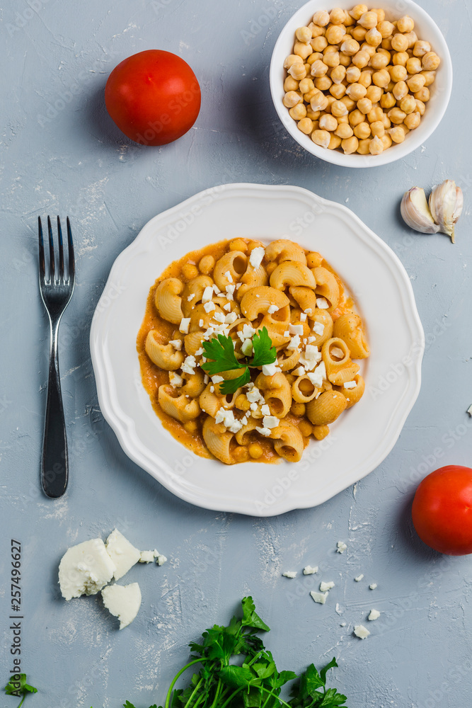 pasta Pipa the rigat with a sauce of chickpeas and tomatoes, sprinkled with feta cheese and cilantro on a white plate on a light grey background high angle