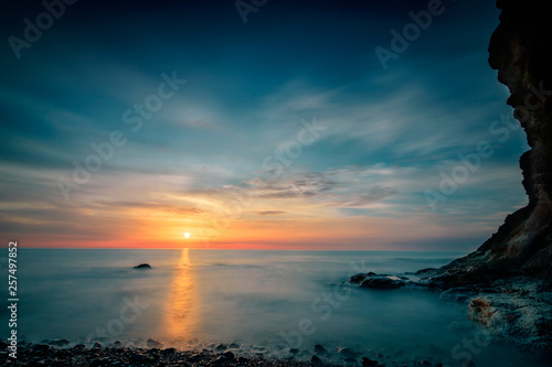 Beautiful sunrise over the more, blue picture look, the sun has just risen and the light is reflected in the duch the long exposure soft water. on the right is a lava rock