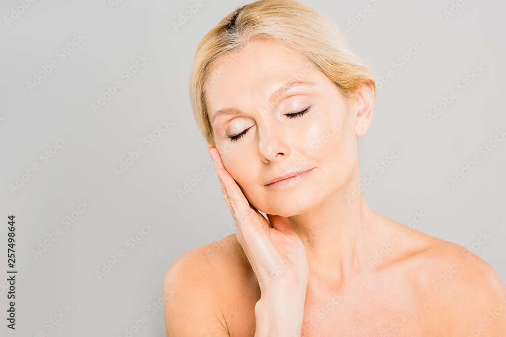 attractive and blonde mature woman with closed eyes touching her face isolated on grey attractive and blonde mature woman with closed eyes touching her face isolated on grey