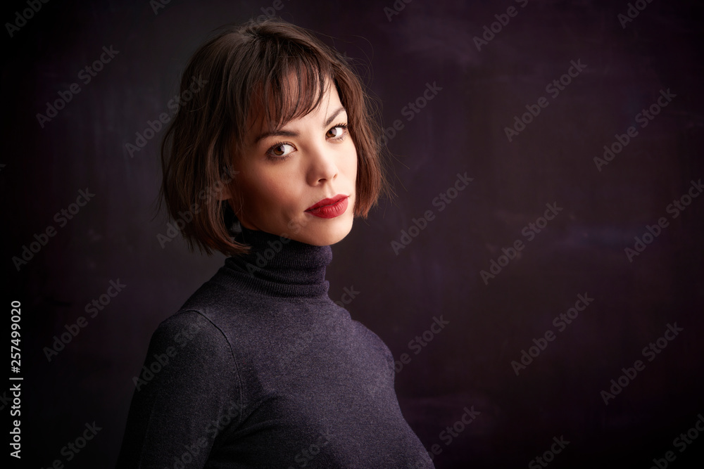 Beautiful young woman standing at dark background and looking at camera