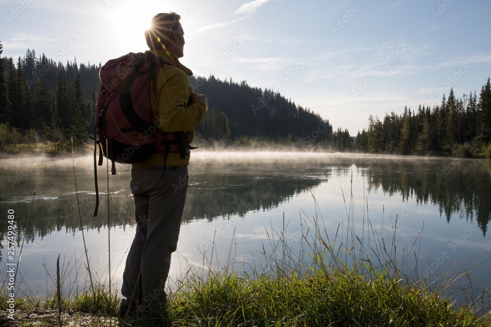 Hiker pauses at edge of mountain lake, sunrise Hiker pauses at edge of mountain lake, sunrise