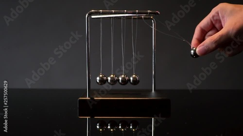 hands pulling ball of metal Newton cradle and observing momentum