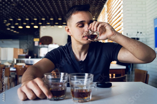 Young man drunk at pub cafe bar holding glass of alcohol drinking whiskey brandy