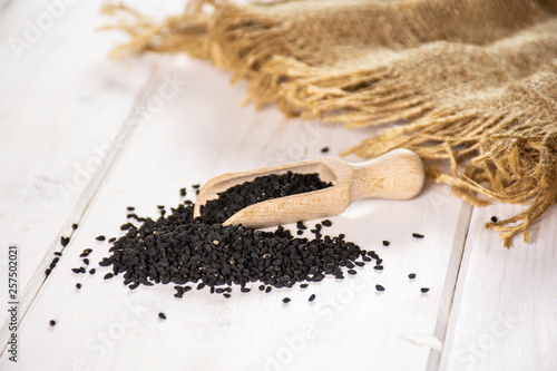 Lot of whole black cumin seeds with wooden scoop and jute cloth on white wood photo