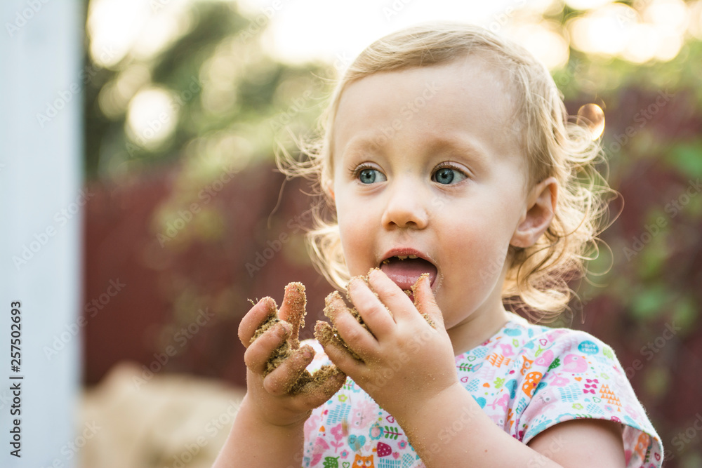 Toddler girl tasting sand from her dirty hands Toddler girl tasting sand from her dirty hands