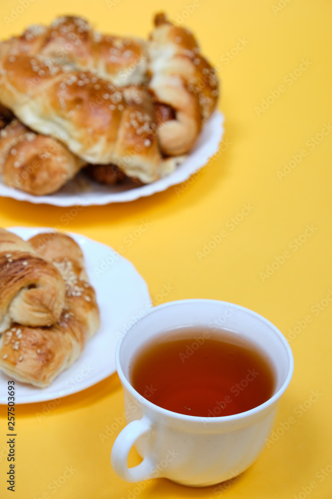 croissants on a white plate with a Cup of tea on a yellow background croissants on a white plate with a Cup of tea on a yellow background