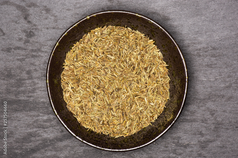 Lot of whole roman caraway seeds in a grey ceramic bowl flatlay on grey stone Lot of whole roman caraway seeds in a grey ceramic bowl flatlay on grey stone