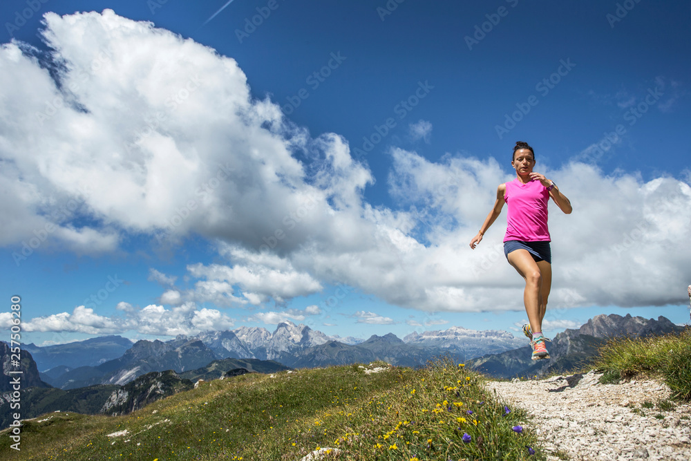 Woman running on Alta Via 1 trail against cloudy sky Woman running on Alta Via 1 trail against cloudy sky