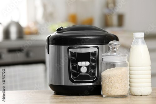 Modern electric multi cooker, rice and milk on table in kitchen