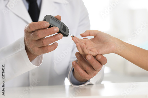 Doctor checking patient's blood sugar level with digital glucometer at table, closeup. Diabetes control
