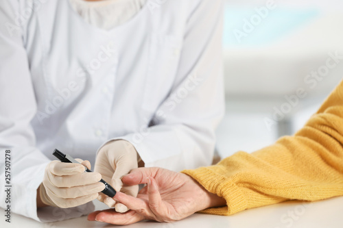 Doctor taking patient s blood sample with lancet pen in hospital  closeup. Diabetes control