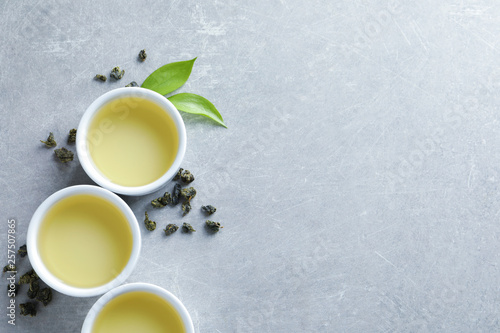 Cups of Tie Guan Yin oolong and tea leaves on grey background, top view with space for text