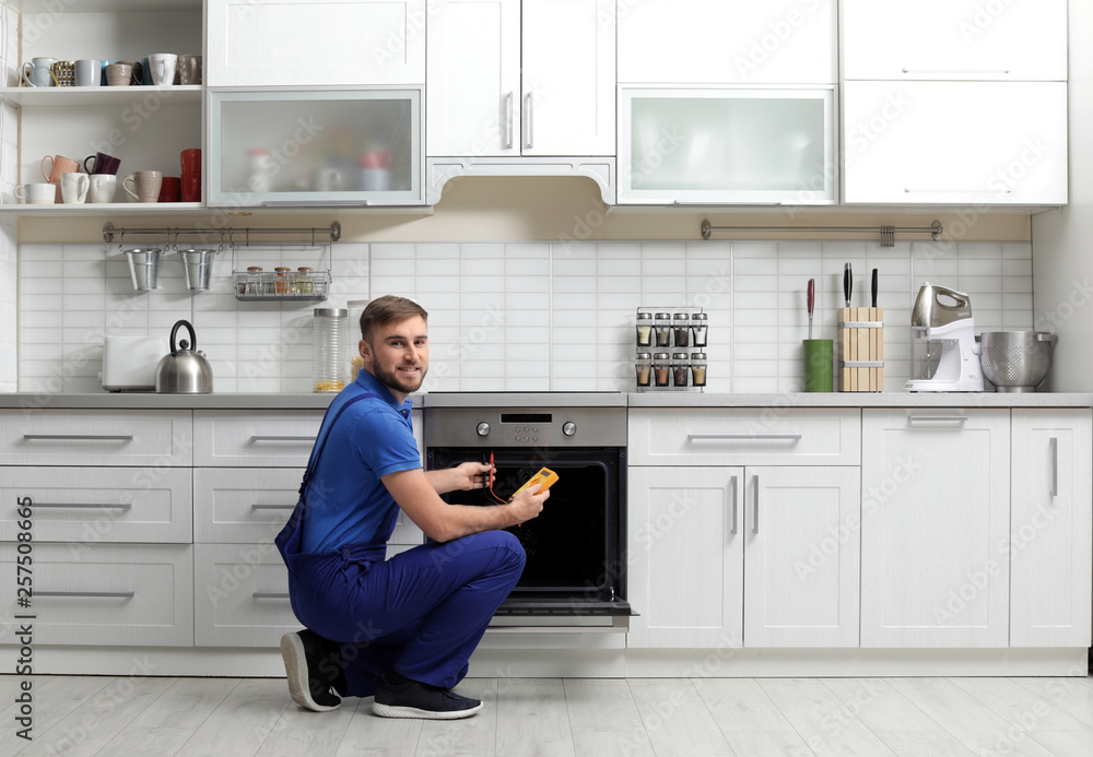 Professional serviceman repairing modern oven in kitchen Professional serviceman repairing modern oven in kitchen