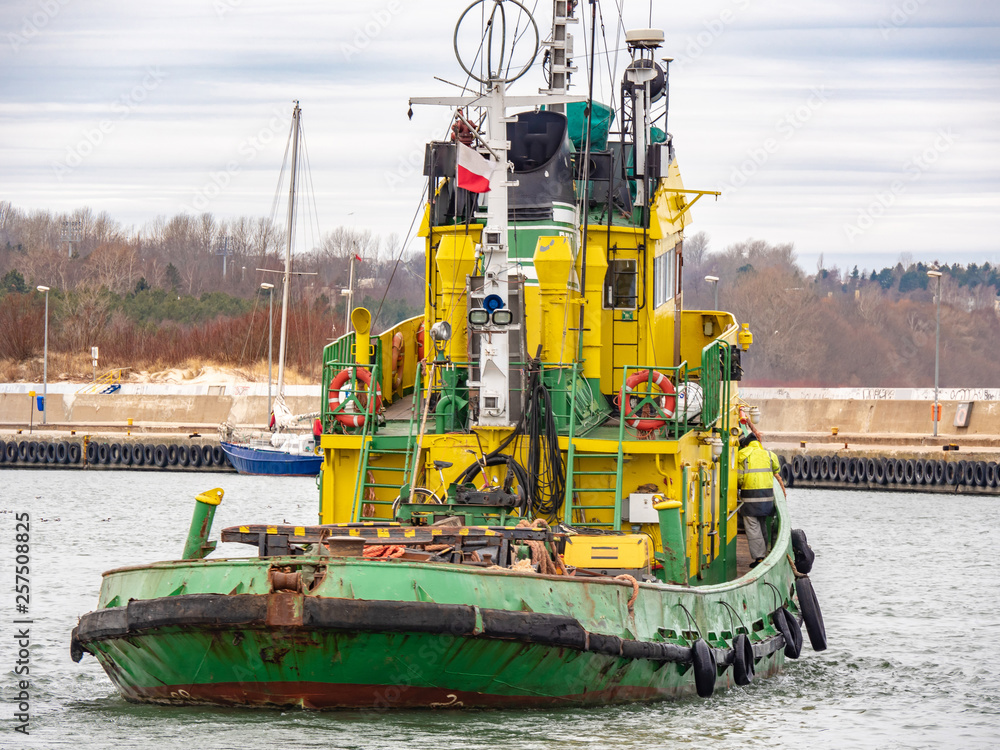 Tug boat, yellow-green color, entering the harbour.