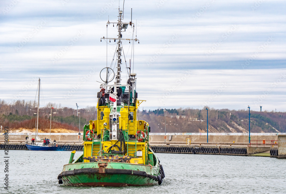 Tug boat, yellow-green color, entering the harbour.