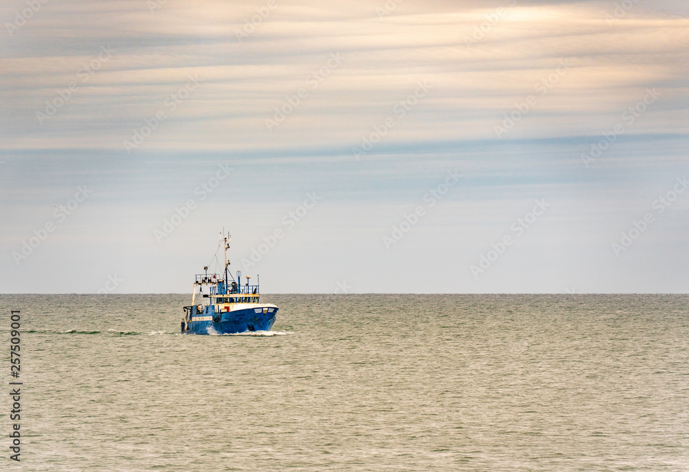 Small single fishing boat at the open sea with scenic sky.