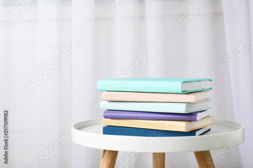 Stack of books on table against curtain. Space for text