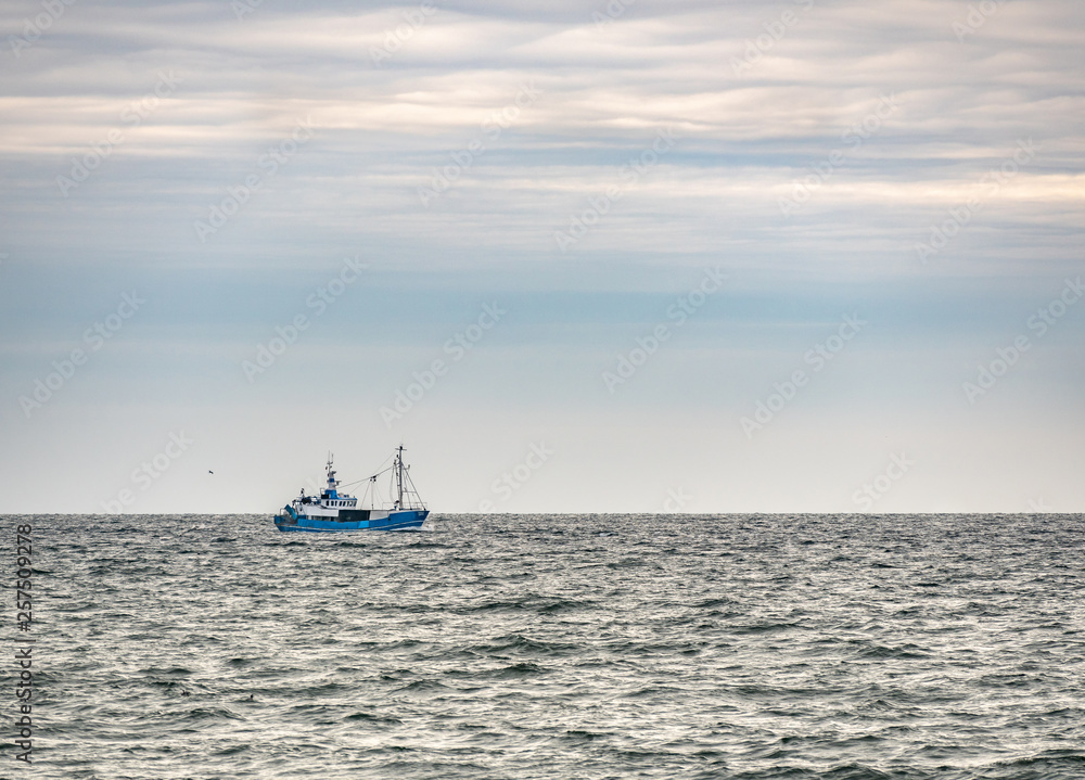 Small single fishing boat at the open sea with scenic sky.