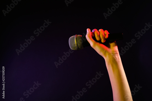 Woman holding microphone on black background, closeup. Space for text