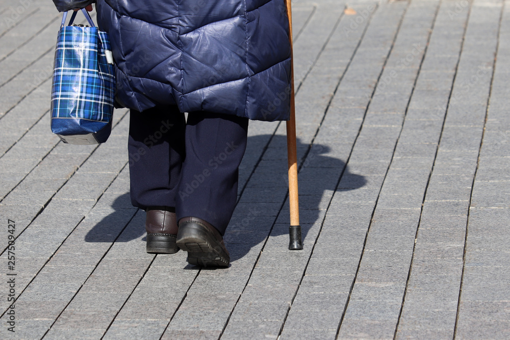 Old woman walking with a cane on a street. Concept for disability, old