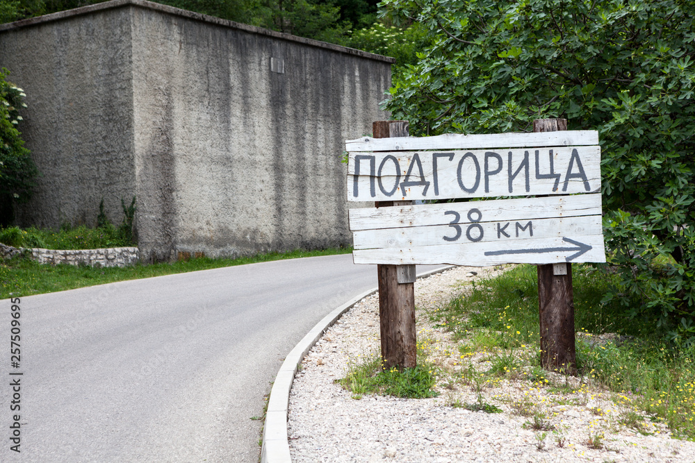 Obraz premium Wooden signpost with direction and distance to Podgorica city in countryside on rural asphalt road. Montenegro. Europe. Podgorica inscription in Montenegrin