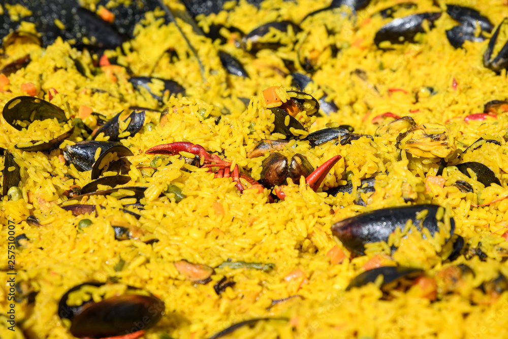 Close up of traditional Spanish paella dish freshly cooked in a large traditional black frying pan at a street food festival, ready to eat seafood, side view Close up of traditional Spanish paella dish freshly cooked in a large traditional black frying pan at a street food festival, ready to eat seafood, side view