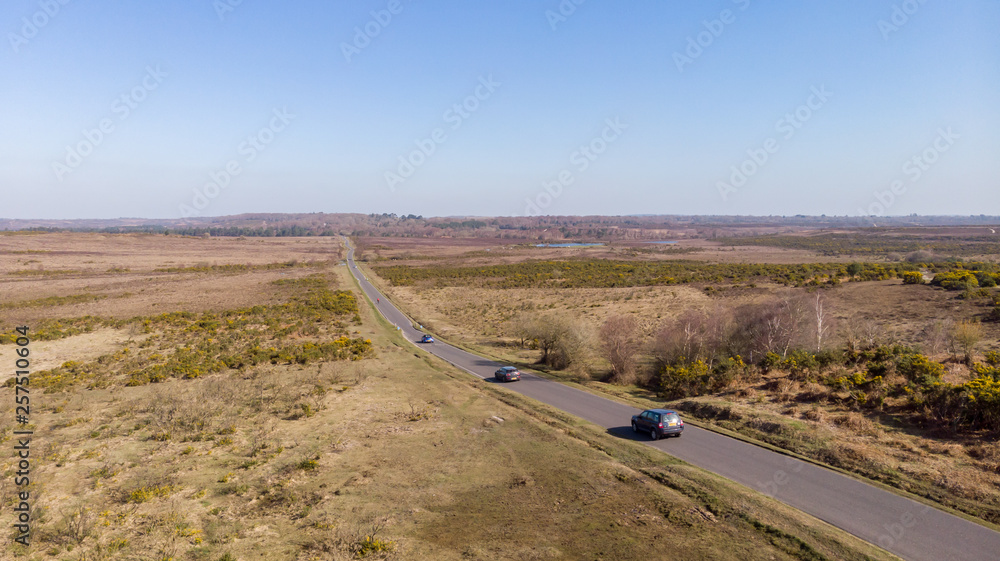 Aerial view of the New Forest National Park with heathland, lake, road, cars and cyclist under a majestic blue sky.