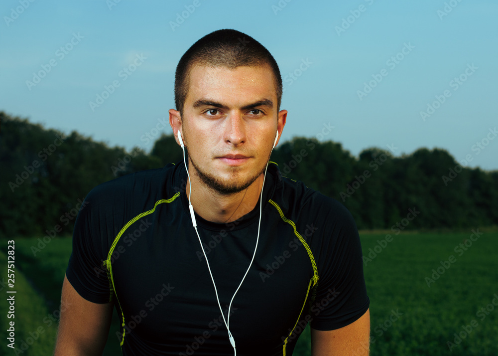 Fototapeta premium guy brunette in gym clothes. training in the field. listening to music on headphones through the phone