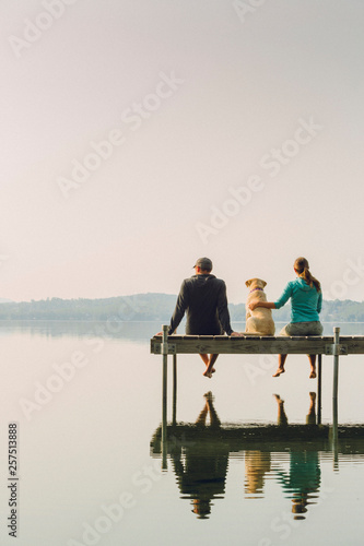 Woman, dog and man relaxing on the end of long lake dock. photo