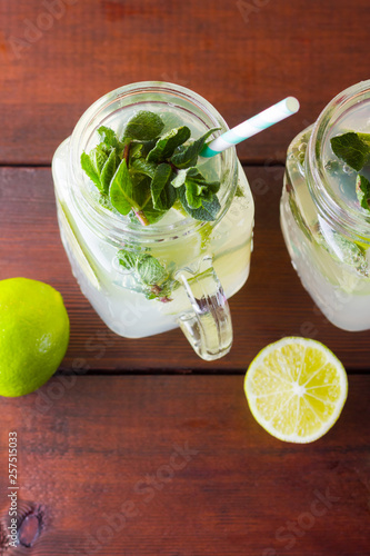 Mojito and mint on wooden background. Refreshing cocktail with lime and fresh mint on wooden boards. Two jars with handles with a summer drink with citrus and ice. Homemade mojito