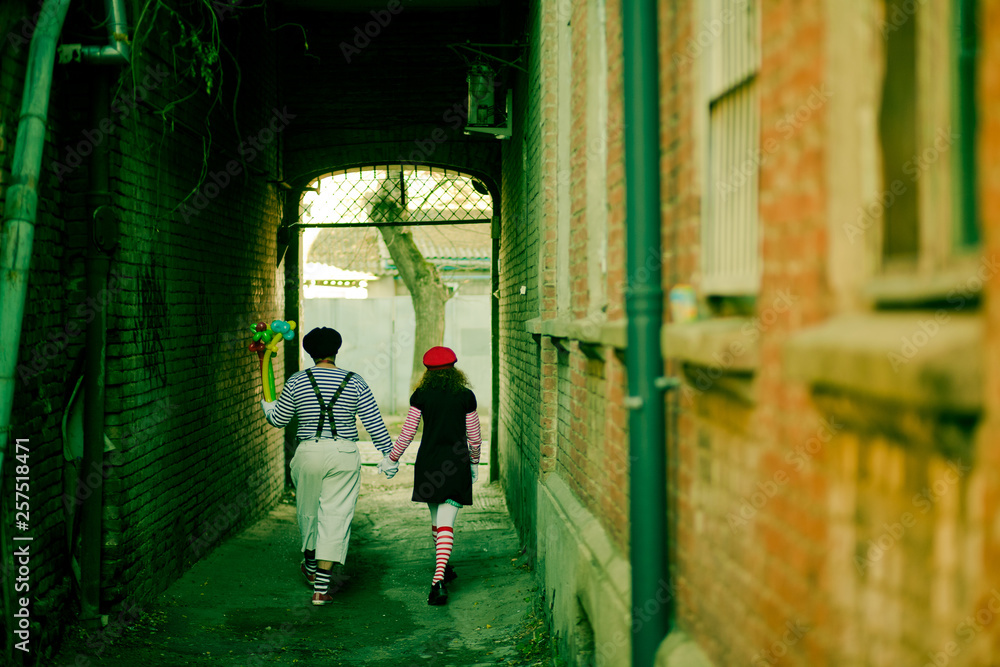 two mimes holding hands go down a narrow alley