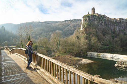 Woman turist poses on the old wooden bridge opposite impressive cliff village Castellfullit de la Roca. photo