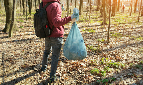 The young guy holding big plastic bag with trash in the forest