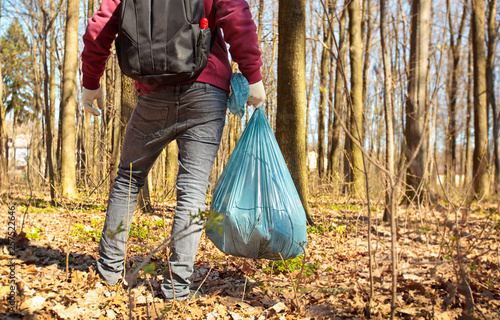 The young guy holding big plastic bag with trash in the forest