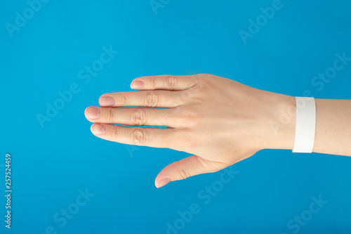 Female hand with empty paper white bracelet on blue background. Music festival branding empty wristband design. Clear sweat band mock up design.