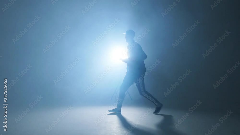 Sporty modern style hip-hop dancer dressed in urban style wear shows his dance on blue studio background, slow motion. Sporty modern style hip-hop dancer dressed in urban style wear shows his dance on blue studio background, slow motion.