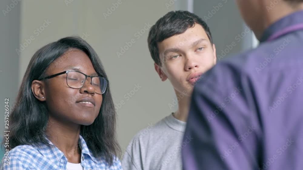 Two college students, African girl and Asian boy asking questions to unrecognizable teacher, listening to his answers with respest and laughing at his jokes Two college students, African girl and Asian boy asking questions to unrecognizable teacher, listening to his answers with respest and laughing at his jokes