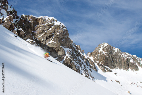 A male backcountry skier with a backpack on makes a powder turn as his dogs follows him in the Beehive Basin near Big Sky, Montana. photo