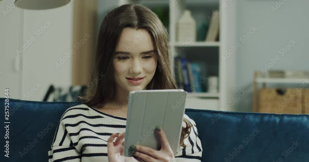 Portrait shot of the young atttractive Caucasian woman using tablet computer and watching some video in the living room. Portrait shot of the young atttractive Caucasian woman using tablet computer and watching some video in the living room.