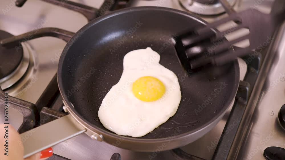 woman in home kitchen frying fried egg in pan for breakfast on old gas stove woman in home kitchen frying fried egg in pan for breakfast on old gas stove