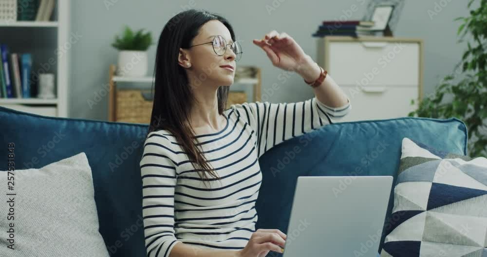 Pretty young Caucasian lady in glasses working as a freelancer at home on the sofa with a laptop computer and thinking. Pretty young Caucasian lady in glasses working as a freelancer at home on the sofa with a laptop computer and thinking.
