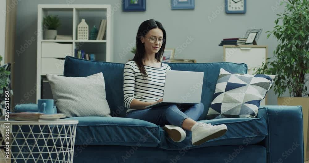 Caucasian young brunette woman in glasses working as a freelancer on the couch in the living room on the laptop computer. Caucasian young brunette woman in glasses working as a freelancer on the couch in the living room on the laptop computer.