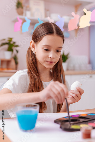 Concentrated brunette little female painting Easter eggs